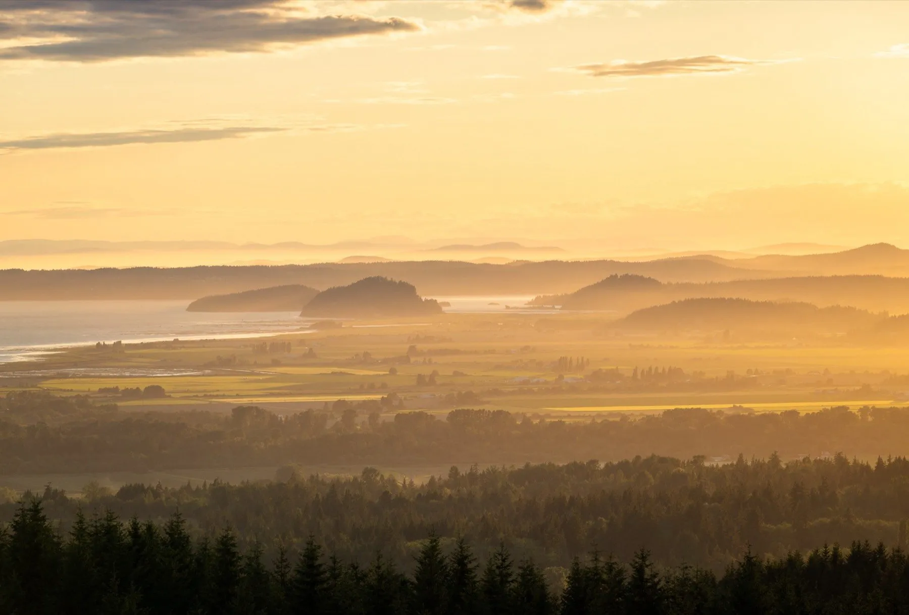 A wide valley at sunset, ridgelines stacked in warm haze under a gold and orange sky.